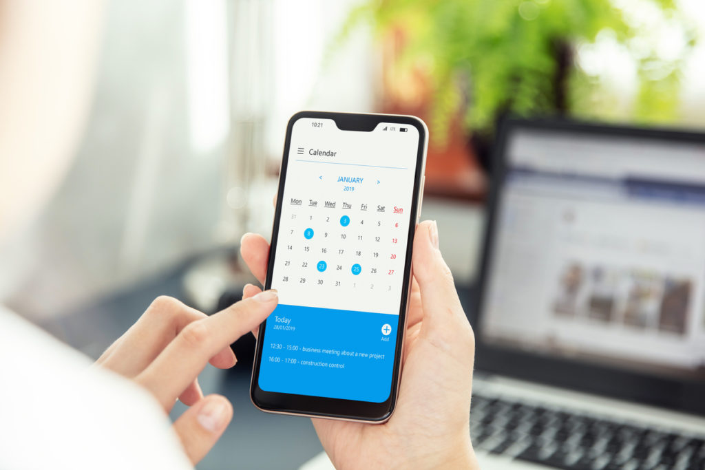 Businesswoman points smartphone screen and checks calendar on application