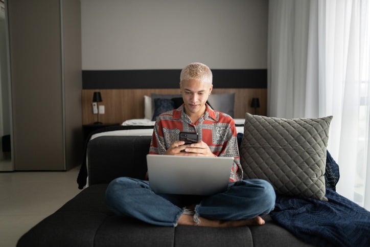 Young man using smartphone and laptop at home