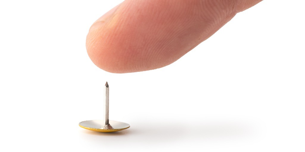 Thumb about to touch the tip of a tack to illustrate customer pain points