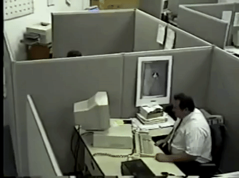 Guy in a cubicle angry at his computer. First, smashing his keyboard, then smacking the computer monitor with the keyboard.