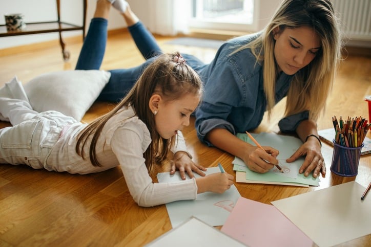 Female babysitter coloring with her young female charge