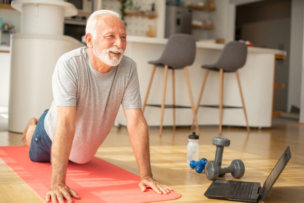 SENIOR MAN DOING HOME WORKOUT IN LIVING ROOM