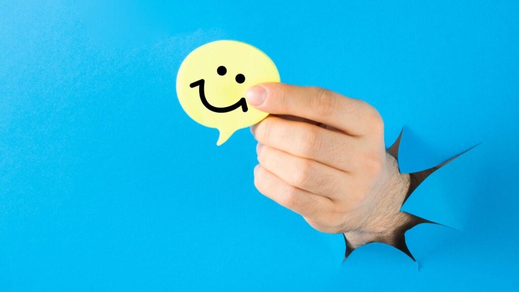 A human hand holding a yellow speech bubble with a smiley face