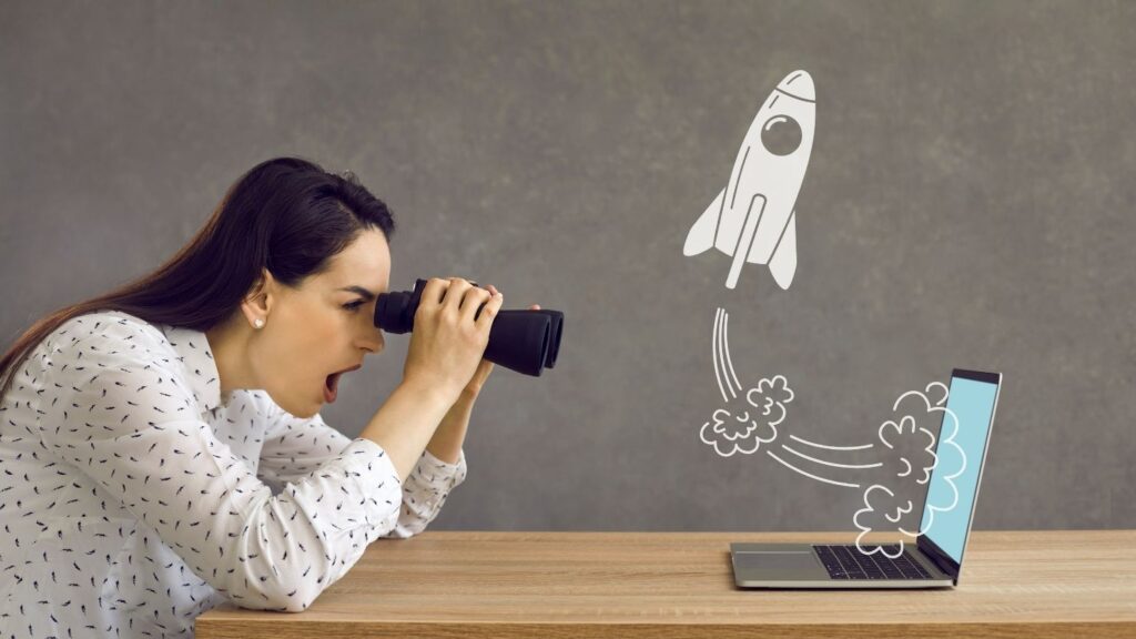 Perfil lateral de uma mulher olhando através de binóculos para um foguete voando na tela do computador de um laptop.