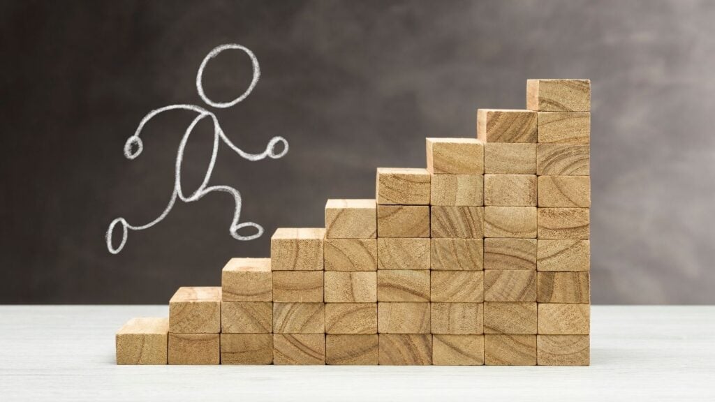 concept of growth shown through wooden steps with a stickman drawing ascending the steps