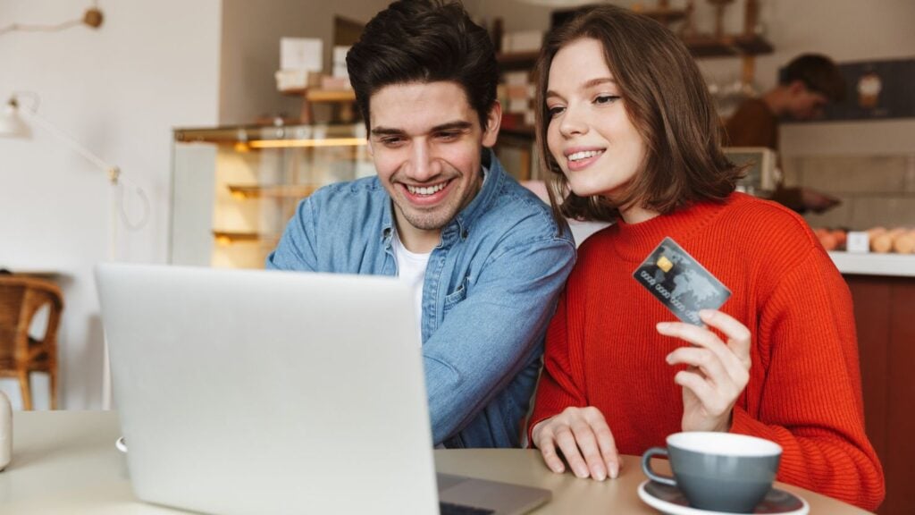 a cheerful young couple holding their credit card while accessing something on their laptop