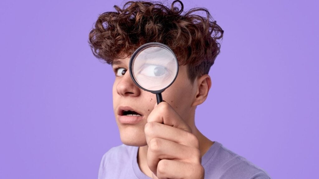 Funny teenager looking through magnifying glass
