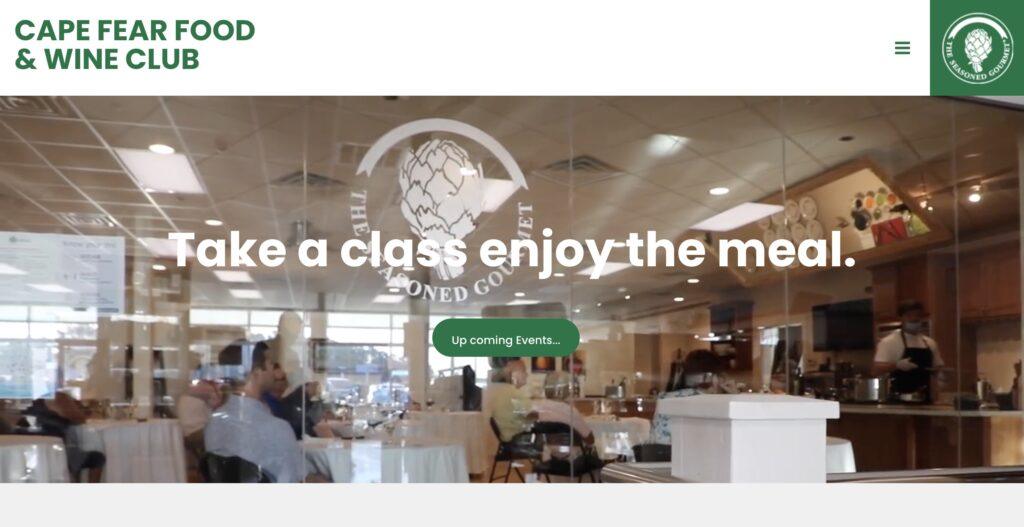 Cape Fear Food and Wine Club Homepage Screenshot | MemberPress Hero banner for Cape Fear Food & Wine Club: restaurant dining room with diners and the text'Take a class enjoy the meal' overlaid on glass dividers.