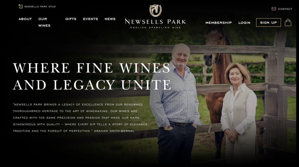 Newells Park Winerey Homepage Screenshot | MemberPress Hero image for Newsells Park site: a man and woman standing beside a wooden fence with a horse in the background, overlaid by the large slogan 'WHERE FINE WINES AND LEGACY UNITE.'