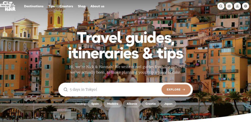 Salt in Our Hair Homepage Screenshot. | MemberPress Hero image of a colorful hillside town with bold white text:'Travel guides, itineraries & tips' overlaid for a travel site homepage.